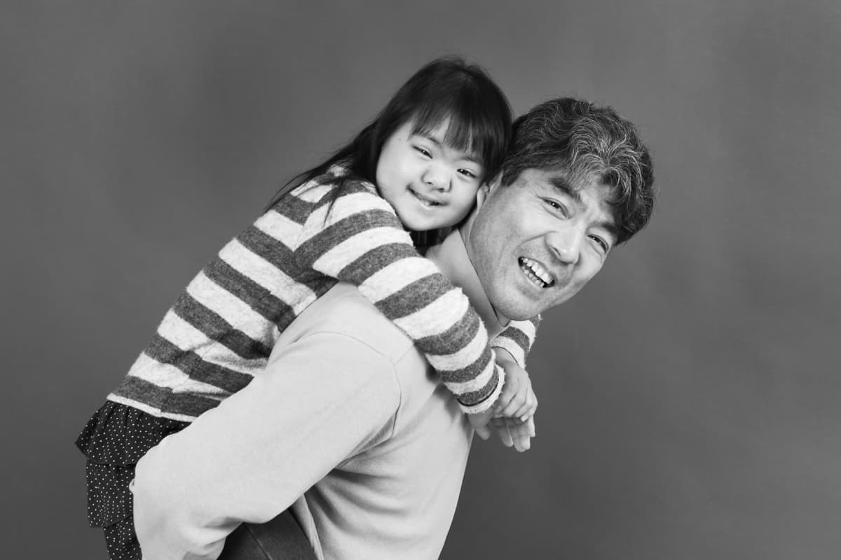 ダウン症女の子を背負う笑顔の父