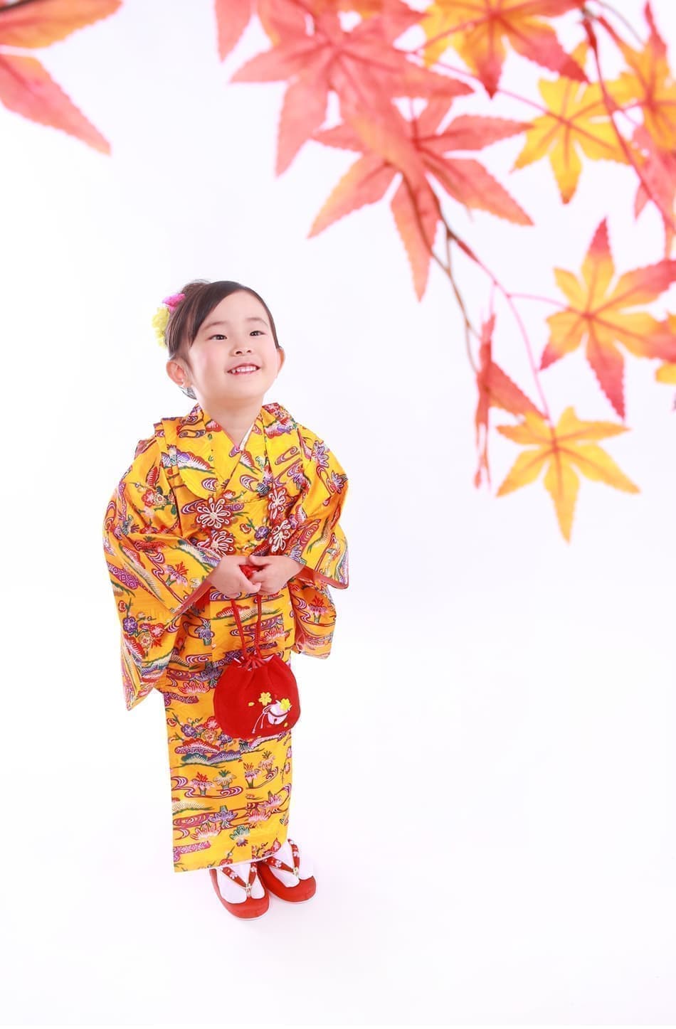 紅葉の下で黄色の着物を着る七五三の女子